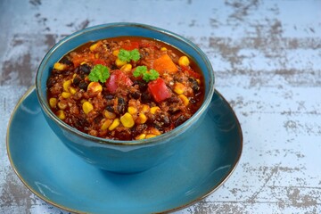 Black bean, quinoa, sweet potato, bell pepper and corn chili in a bowl garnish with parsley