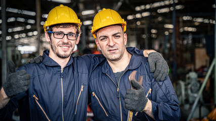 Two workers in blue jumpsuits with yellow hard hats smiling. Confident mechanics ready for work.	
