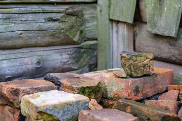 Old red bricks, burnt and overgrown with moss, are stacked against a log shed.