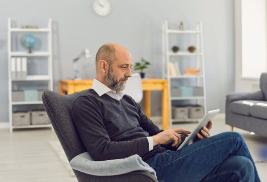 Senior man with tablet writing text online, chatting with family, consulting doctor or watching webinar at home