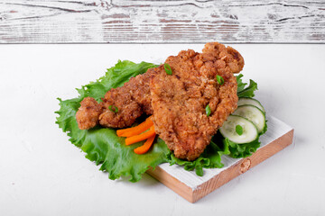 Wiener Schnitzel breaded and served with fresh vegetables on the wooden board