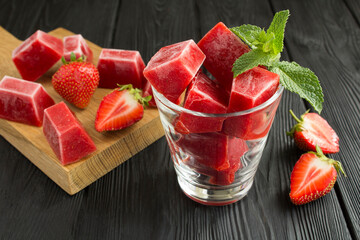Ice cubes with strawberry in the glass on the black wooden background