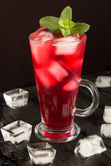 Cold pink lemonade with ice in the glass on the black background. Closeup. Location vertical.
