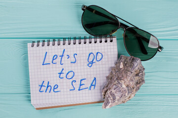 Travel concept made of sea shell and sun glasses on blue background. Let's go to the sea written on...