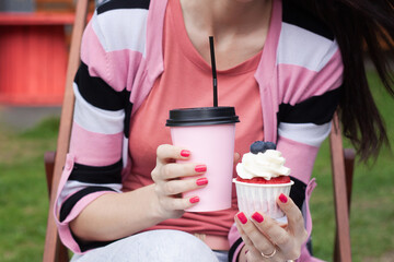 Pink disposable coffee Cup and cake in women's hands on the street.
