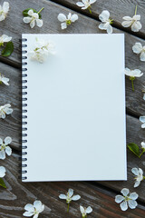 An empty notebook covered with cherry flowers on a wooden texture. Blank space where you can put your text.