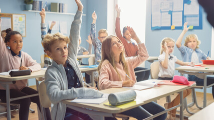 Elementary Classroom of Children Listening Attentively to their Teacher Giving Lesson. Everybody...