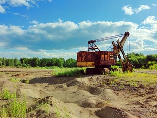 Obraz premium old rusty excavator on a sand quarry on a background of green forest and blue sky on a sunny day
