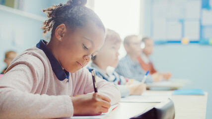 In Elementary School Classroom Black Girl Writes in Exercise Notebook, Taking Test. Junior...