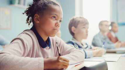 In Elementary School Classroom Black Girl Writes in Exercise Notebook, Taking Test. Junior...