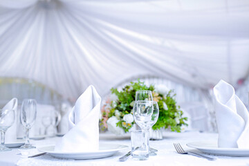 Wedding table with a white tablecloth in a white outdoor tent