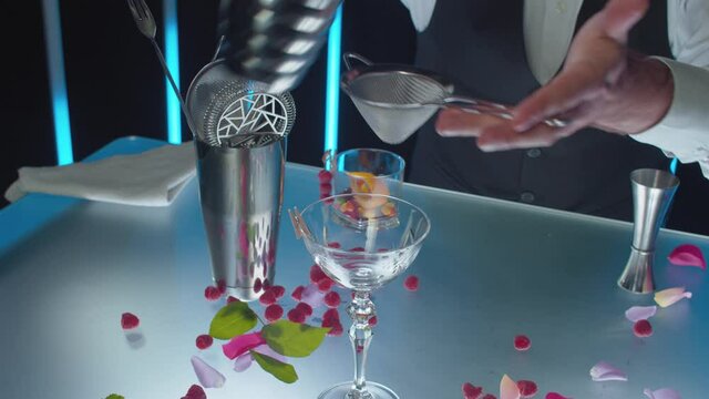Bartender preparing Red Dress cocktail. Close up bartenders hands pouring a cocktail from shaker through a strainer and decorating it with orange zest. Motion control system