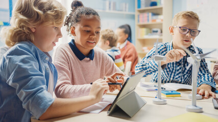 In the Elementary School: Class of Smart Young Children Work as a Team Using Tablet Computers to Program Wind Turbines. Classroom with Kids Learning about Eco-Friendly Forms of Renewable Energy