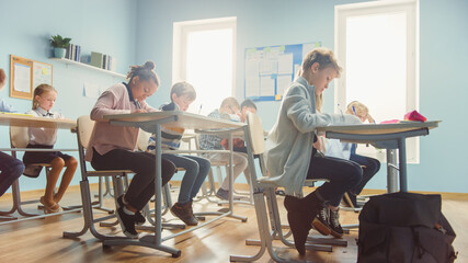Shot of a Classroom Full of Diverse Children. In Elementary School Group of Smart Multiethnic Kids Writing in Exercise Notebooks and Learning. Low Angle Side View Shot. - obrazy, fototapety, plakaty