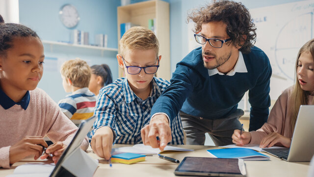 Elementary School Classroom: Enthusiastic Teacher Using Tablet Computer Explains Lesson to Brilliant Young Children. Kids Learning Programming Languages, Internet Safety and Software Design