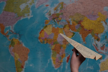 Fototapeta na wymiar symbol of unattainable impossibility limitation journeys. hand holding a paper airplane on the background of the world map. the inability of the limited ban on travel from coronavirus
