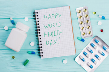 Different pills with notebook and blister packs on blue background. Congratulations on world health day.