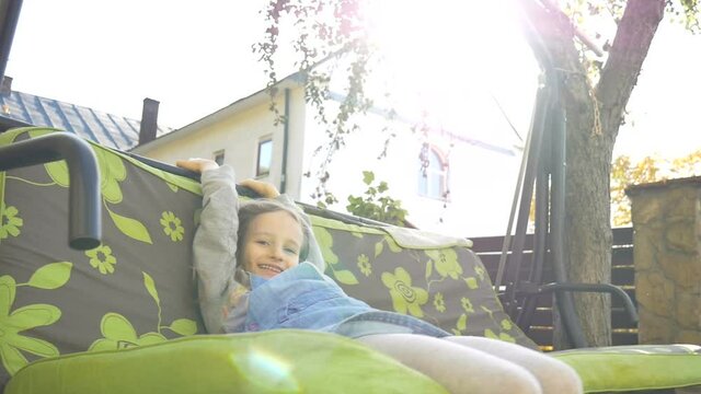 Little child blond girl having fun on a swing outdoor during summer sunny day on playground in the garden, happy childhood concept