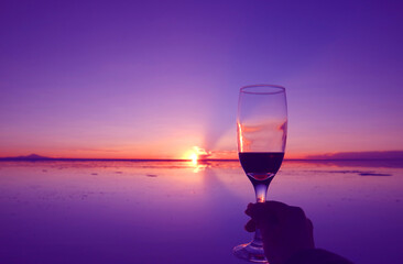Pop art style purple colored hand holding liquor glass against sunset over the famous flooding salt flats of Salar de Uyuni in Bolivia
