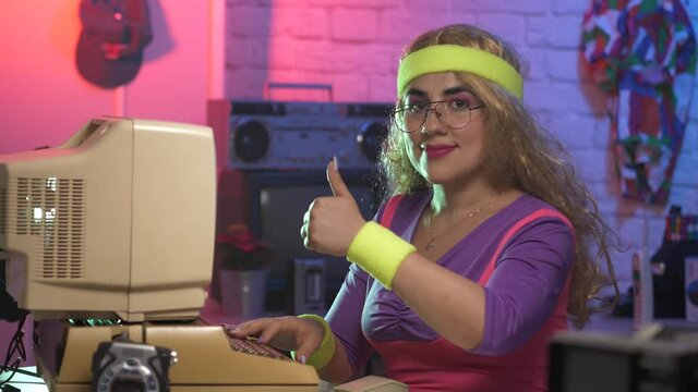 Vintage style girl from the 80s 90s using an old computer and giving a thumbs up to the camera smiling. Retro style scene.