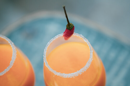 Top Down View Of Cocktail Glasses With Orange, Mango And Red Chilli Exotic Drinks In A British Summer Home Garden. 