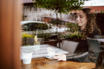 Cute brunette, curly girl sitting in a cafe, drinking coffee and juice.