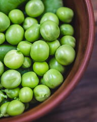 fresh green peas in a brown bowl on a wooden table