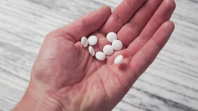 White medical pills falling slowly in a pile on the palm of his hand close-up. Light wooden background. Medical concept