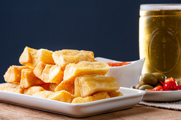 .Fried manioc. Traditional Brazilian food dish. Accompanied by pepper jam, olives and pepper pout. Glass of beer. Selective focus. Space for text