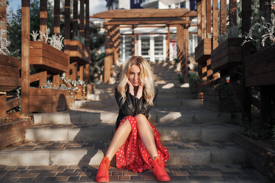 Blond young woman on red dress sitting on stairs looking to the camera