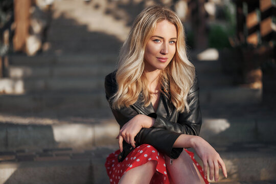 Blond young woman on red dress sitting on stairs looking to the camera