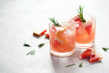 Refreshing grapefruit cocktail with ice and rosemary on a grey background.