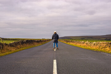 Obraz premium Photo of a man with a winter coat standing in the middle of the road surrounded by nature in the UK