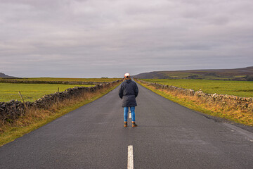Photo of a man with a winter coat standing in the middle of the road surrounded by nature in the UK