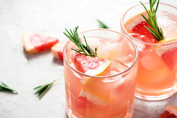 Refreshing grapefruit cocktail with ice and rosemary on a grey background.