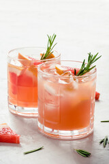 Refreshing grapefruit cocktail with ice and rosemary on a grey background.