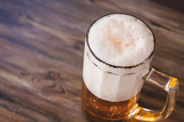 Mug of beer with foam on a wooden table copy space. Cold beer.