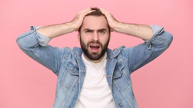 Shocked fun surpised bearded young man guy 20s years old in denim jacket white t-shirt isolated on pastel pink background studio. People lifestyle concept Looking camera put hands on head say ask what