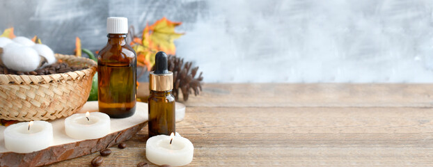 Aromatherapy concept with essential oil bottle, cotton flowers, burning candles on wooden background. Autumn spa still life composition. Hygge. Copyspace.