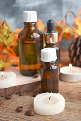 Fototapeta na wymiar Close up autumn spa concept with essential oil bottle, dried leaves, burning candles on wooden background. Aromatherapy still life composition. Organic cosmetic..