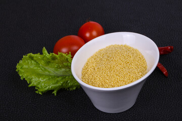 Raw couscous in the bowl served salad leaves, tomato and pepper