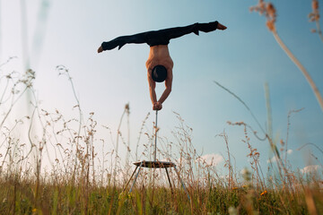 A man of athletic build performs complex gymnastic exercises in a field at sunset.