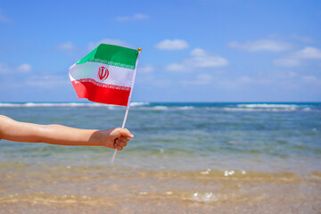 Hands of kid girl holding Iran flag against the sea horizon. 21th of February Independence day of Iran, concept.