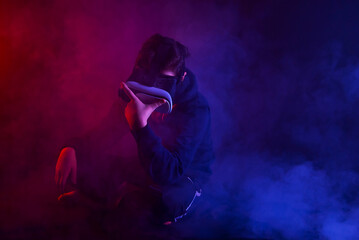 Guy in a virtual reality helmet with headphones. Thick smoke with red and blue tinges in the background. A man plays a game. Dramatic contrasting shadows on the face as an artistic effect.