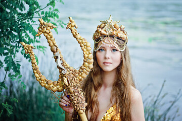 Fantasy woman real mermaid with trident myth goddess of sea with golden tail sitting in sunset on...