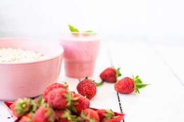 Fresh strawberry yogurt with berries around on a white wooden background. A pink shake in a glass, next to it is a pink cup with Hercules flakes, and red strawberries lie in a red star-shaped plate