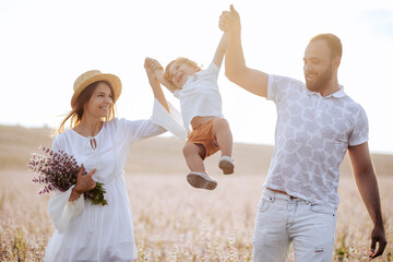 Happy family portrait outdoor at the sunset time. People having fun on the field. Concept of friendly family and of summer vacation. Parents and son spending good time. White dress. Straw hat. Kissing