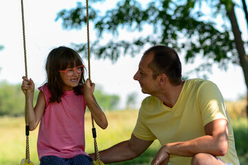 Father spends time on swing with his cute daughter in forest.