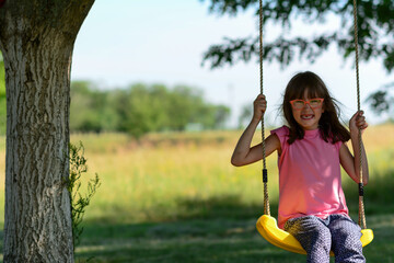 A girl in the forest swinging on a swing. Girl in a pink shirt with long hair. Image with selective focus. Little smiling girl swinging on a swing outdoors in the forest.