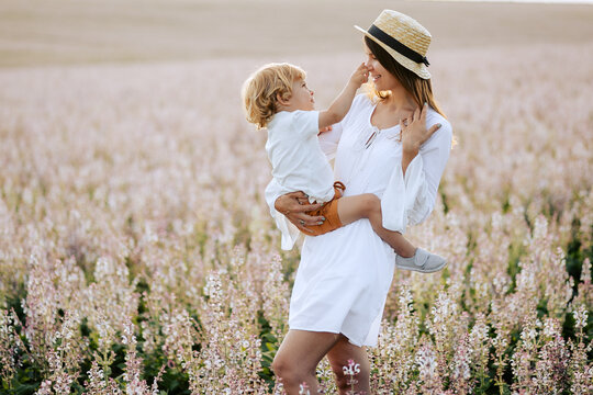 Mother and son playing in the field. Beautiful young woman wearing a white dress and straw hat playing with her little boy outside.